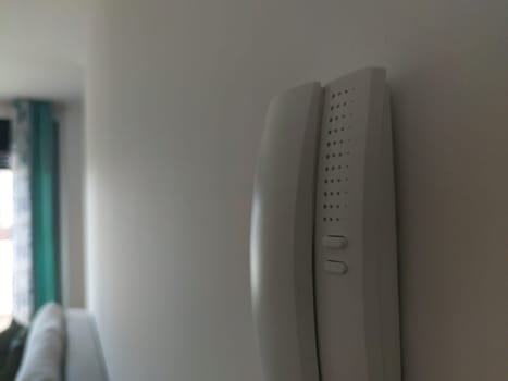 Intercom attached on the wall of living room. Window light at bottom. Blurred foreground