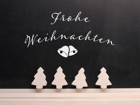 Chalkboard with the German inscription Merry Christmas and decorative wooeden tree shapes