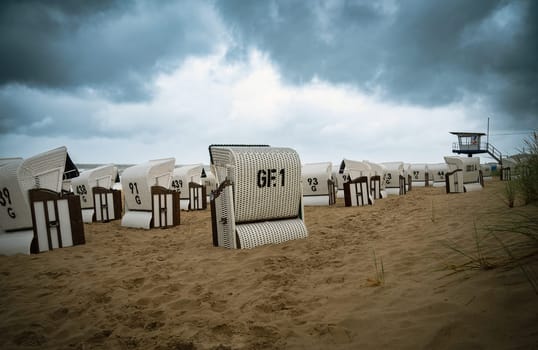 Roofed wicker beach chairs at the baltic sea beach, coast at the island of Usedom in Germany, storm and rain over the brackish water, high waves, storm warning