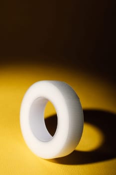 Flexible plastic tape for eyelash extension procedure, illuminated from above, lying on yellow table. Tool with durability, ensuring lashes remain properly positioned throughout procedure. Vertical.