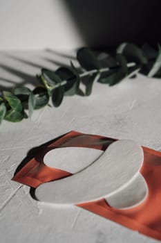 Clean thin patches using for isolating lashes and applying on lower eyelids in process of eyelash extension procedure lying on red wrapping on white table in front of green stem of plant. Vertical.