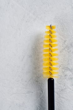 Yellow disposable eyelash extension brush isolated against white wall. Tool with fine bristles allowing for precise and controlled lash placement, ensuring achievement flawless result. Vertical.