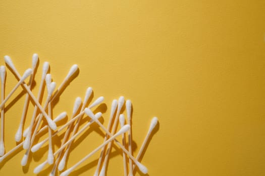 Bunch of disposable cotton buds with beige bamboo sticks isolated on bright yellow background, positioning in left lower corner. Consumable using for assisting throughout cilia extension procedure.