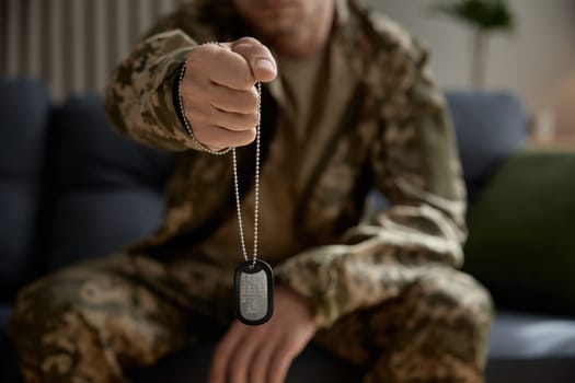 Closeup military hand holding metallic badge dog tag with qr code. Mourning for dead brothers in war