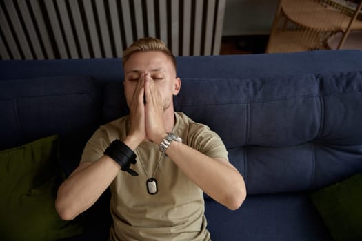 Depressed soldier suffering from military PTSD sharing his concerns covering face with hands while sitting on sofa at therapy session. Veteran rehabilitation concept
