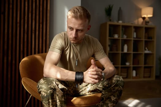 Portrait of military man being deep in thoughts feeling sorrowful and loneliness sitting on chair at home. Mental disorder and ptsd symptom