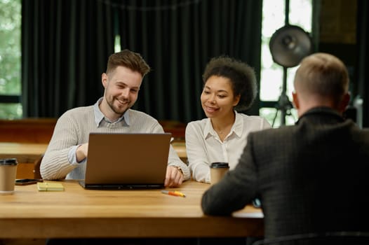 Happy multiethnic business team talking, working together at coworking office open space. Corporate collaboration co-working concept