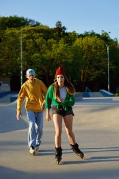 Cool teen male and female friends riding on roller skates in park. Hobby summer activity concept