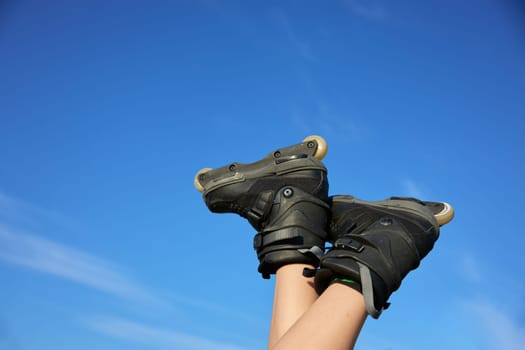 Human feet wearing roller skates in air over summer blue sky. Sport and hobby activity during summertime vacation