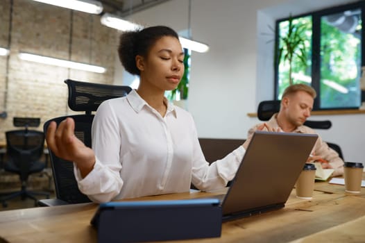 Businesswoman office worker relaxing doing yoga sitting front of laptop computer at coworking open space