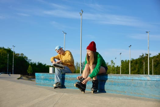 Preparation for training in park. Young people enjoying skating wearing rollers on feet while sitting on bench