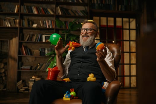 Happy smiling rich elegant senior businessman with toys sitting on armchair laughing loudly having fun