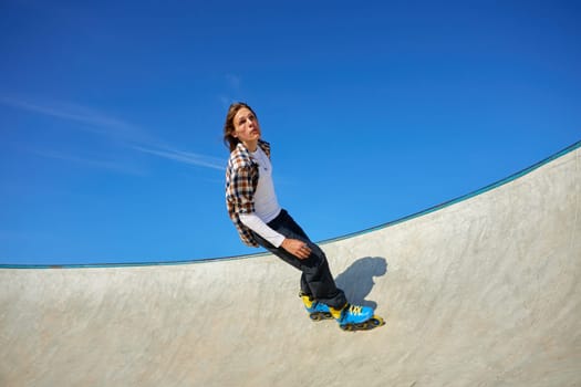 Teenager guy wearing roller skates performing extreme wall-ride element in skate park