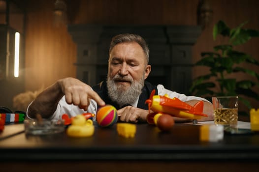 Portrait of thoughtful senior businessman playing toys while rest at workplace in home office. Elderly male having fun enjoying stress relief entertainment