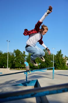 Young guy wearing rollerblades jumping from handrail on outdoor rollerdrome. Active recreation in skating park