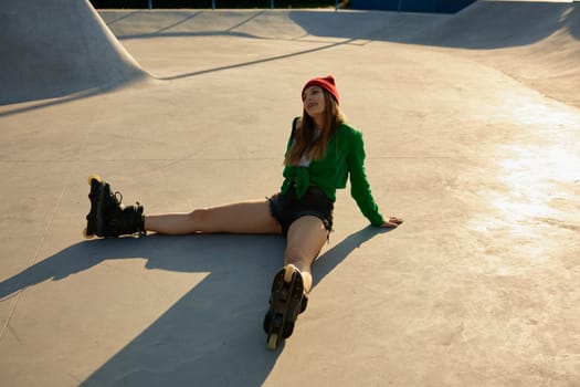 Tired but satisfied teenager girl wearing roller skates sitting on asphalt rollerdrom. After active sport training
