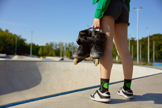 Closeup female teenager with rollers standing front of skating ramp. Preparation for sports training with professional equipment