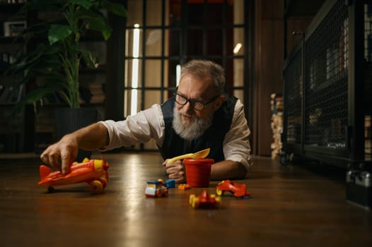 Funny successful senior businessman playing toys while lying on floor at home office. Relax time after work concept