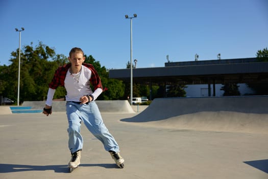 Trendy fashioned teenage guy rollerblading at urban skating park. Extreme sports and active recreation