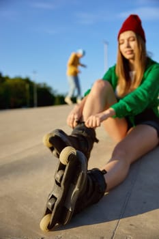 Happy relaxed woman smiling while sitting on rollerdrom. Teenager female rollerskater rest after free riding activity