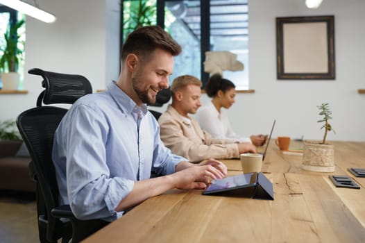 Colleagues working in coworking open office space. Focus on man worker using mobile tablet and smiling feeling satisfaction of getting good job result