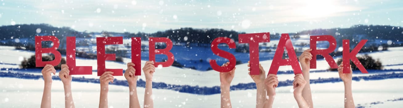 People Or Persons Hands Building German Word Bleib Stark Means Be Strong. White Winter Background With Snowflakes And Snowy Landscape.