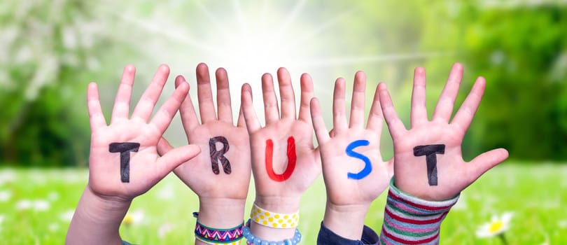 Children Hands Building Colorful English Word Trust. Sunny Green Grass Meadow As Background.
