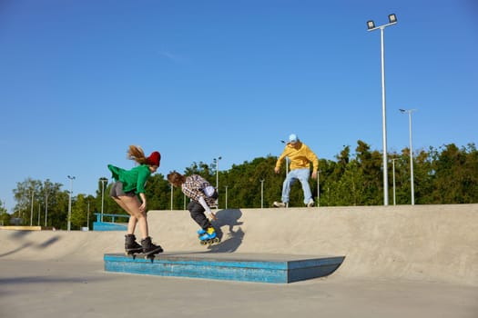 Teenager friends wearing roller blades having recreation time in urban skate park. Happy healthy weekend for teens