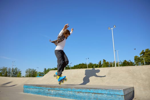 Young guy wearing inline skates doing balancing stunt at skateboard park. Extreme sports event for teenagers