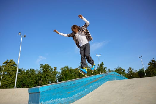 Young teen wearing inline skates doing balancing stunt at skateboard park. Extreme sports event for teenagers