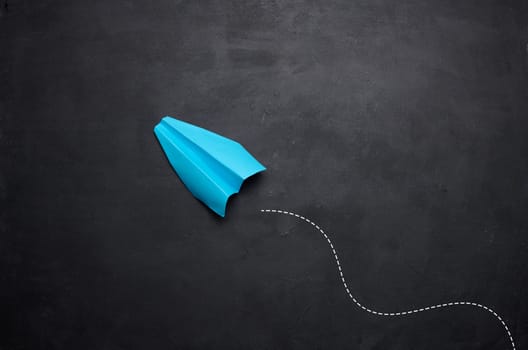 Blue paper airplane on a black background, travel concept, top view. Copy space