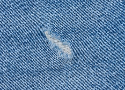 Fragment of blue jeans fabric with a hole, full frame, close up