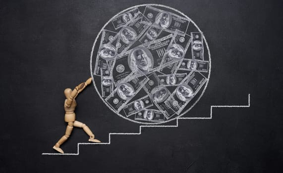 A wooden mannequin rolling a large ball with drawn dollars down the stairs, symbolizing the concept of wealth and hard work towards achieving goals. Inflation and increase in money supply