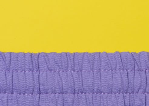 Fragment of purple fabric with an elastic band on a yellow background