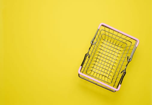 Empty miniature shopping cart on a yellow background, top view, representing the concept of shopping