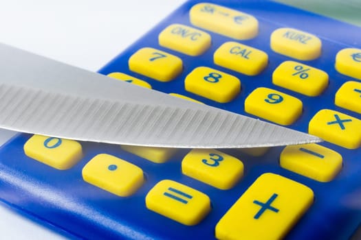 Knife blade placed on euro coin, calculator. Concept cut rates, money business, crime. Macro.