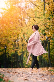 Ballerina dancing in nature among autumn leaves in fair coat.
