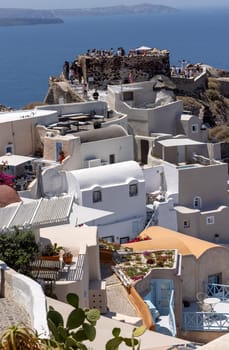 Oia, Santorini, Greece - July 3, 2021: Whitewashed buildings and the ruins of Castle of Agios Nikolaos on the edge of the caldera cliff, Oia village, Santorini, Greece