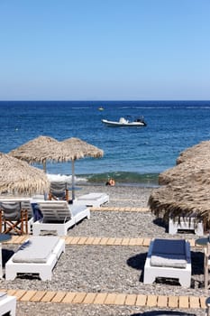 Kamari, Santorini, Greece - June 30, 2021: Sun loungers on the black volcanic beach of Kamari in Santorini. Cyclades, Greece