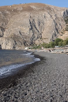 Kamari, Santorini, Greece - July 3, 2021: Sun loungers on the black volcanic beach of Kamari in Santorini. Cyclades, Greece