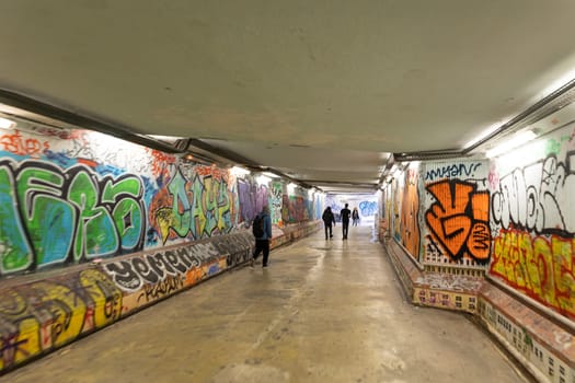 February 21, 2023 Lisbon, Portugal: people walk through an underground passage with graffiti-painted walls. Mid shot