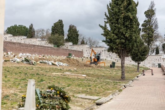 February 22, 2023 Lisbon, Portugal: Alto de Sao Joao Cemetery - excavator digs up the earth for the grave. Mid shot