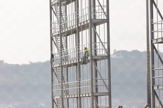 Construction site - a black worker sits at the height of the building frame. Mid shot
