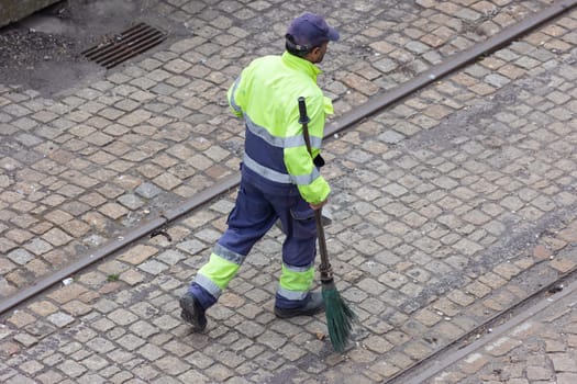A worker reflective vest walks on the street with a broom. Mid shot