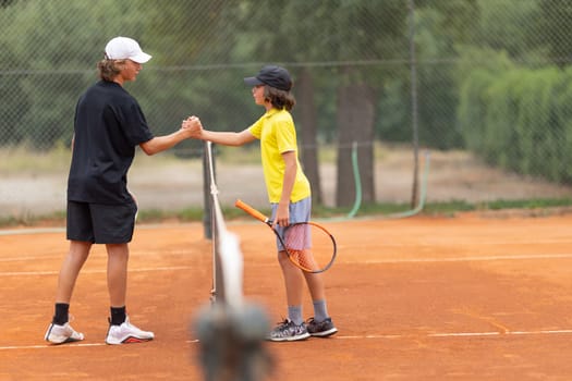 Two boys shake hands above the net on the tennis court. Mid shot