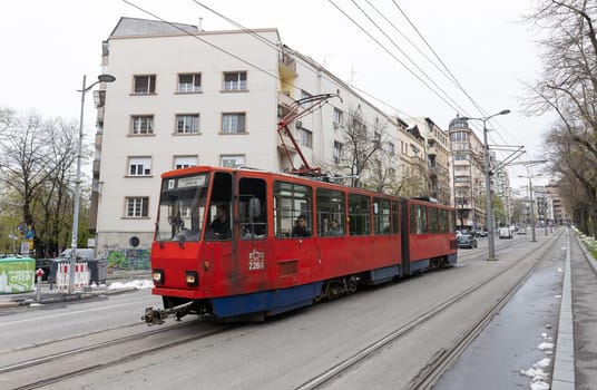 5 April 2023 Belgrade, Serbia: a red old tram rides along the tracks on the street. Mid shot