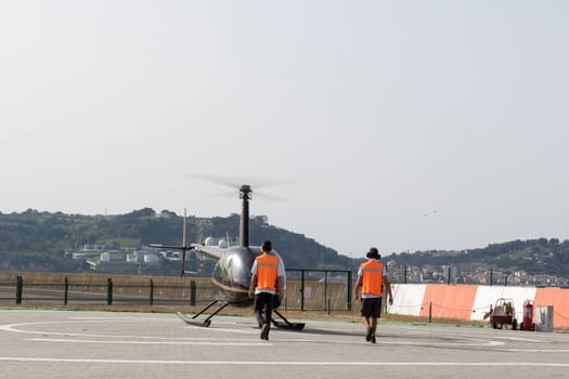 Two people in reflective vests walk to the helicopter. Mid shot
