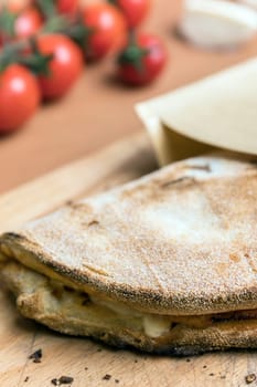 Italian food, closed calzone pizza on rustic wooden background. On blurred background small red tomatoes. Selective focus