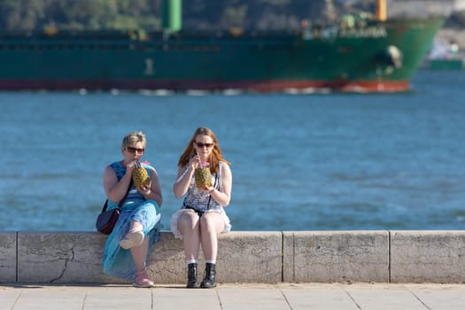 11 April 2023 Lisbon, Portugal: two women different ages tourists drinking cocktails on waterfront. Mid shot