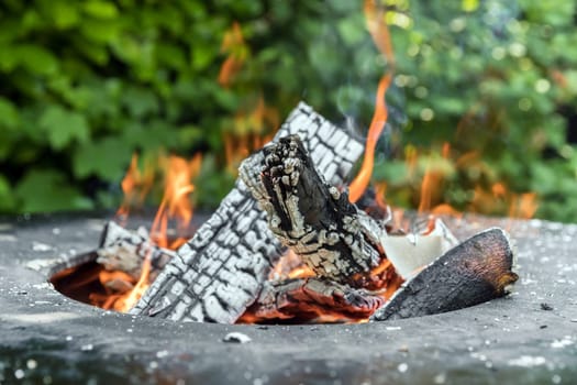 Close up shot of log pieces and fire wood, charcoal and ashes burning in hot oranges flames in an brazier.